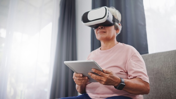 senior Asian woman using a tablet to control content on VR glasses at home,